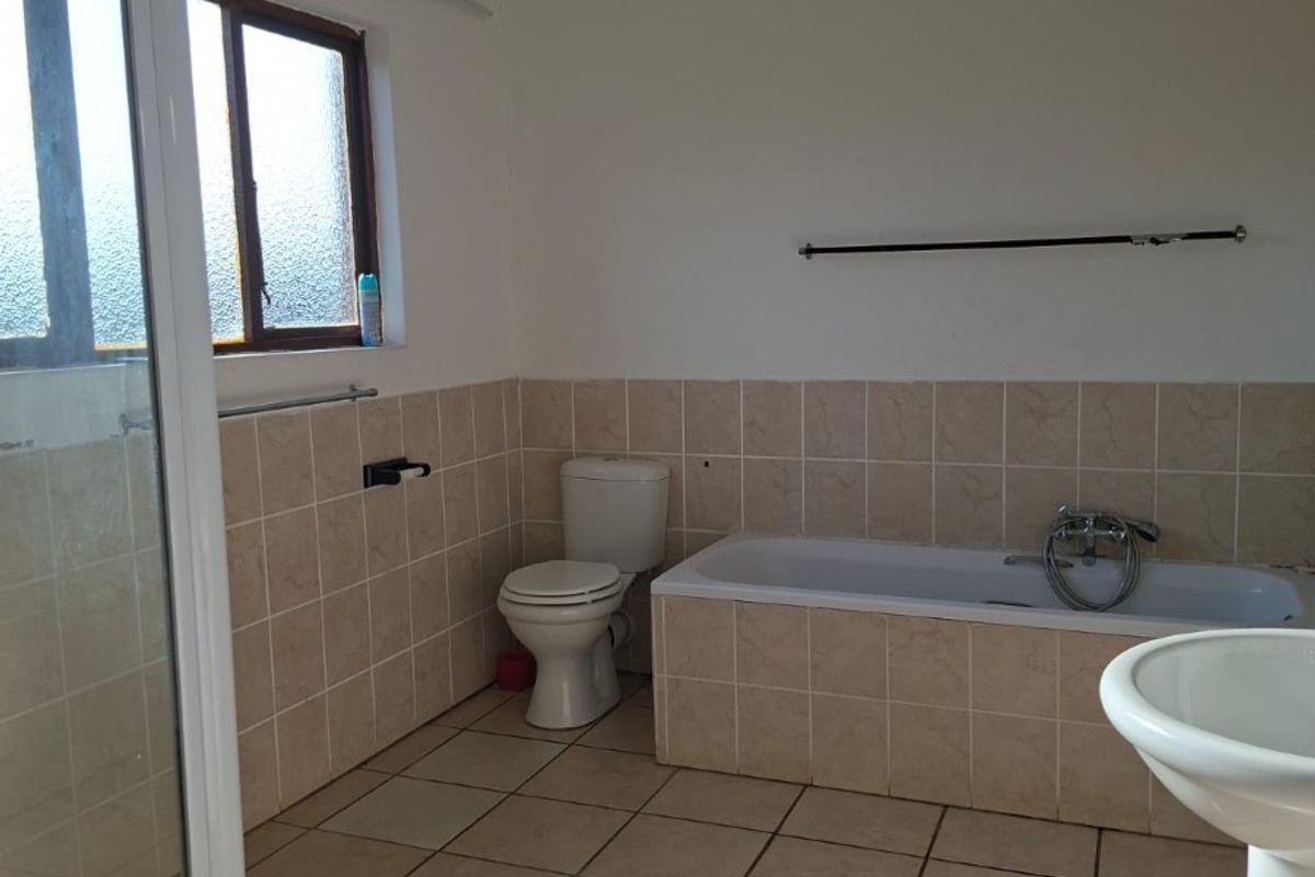 A functional bathroom featuring a shower enclosure, bathtub, pedestal basin, and toilet with neutral tiled finishes.