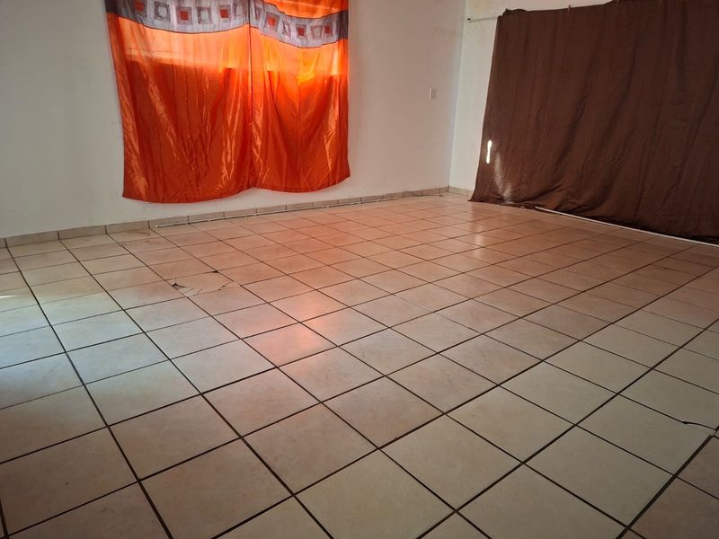 An empty living room featuring ceramic floor tiles, showing signs of wear including a cracked tile.