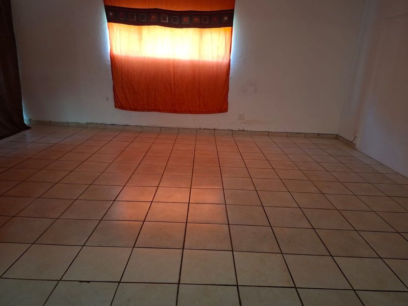 An empty living area featuring neutral ceramic floor tiles and plain white walls, ready for personalization.