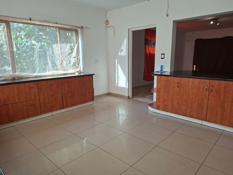 An empty kitchen area featuring built-in wooden cabinetry, dark granite countertops, and tiled flooring, requiring minor cosmetic updates and electrical finishing.