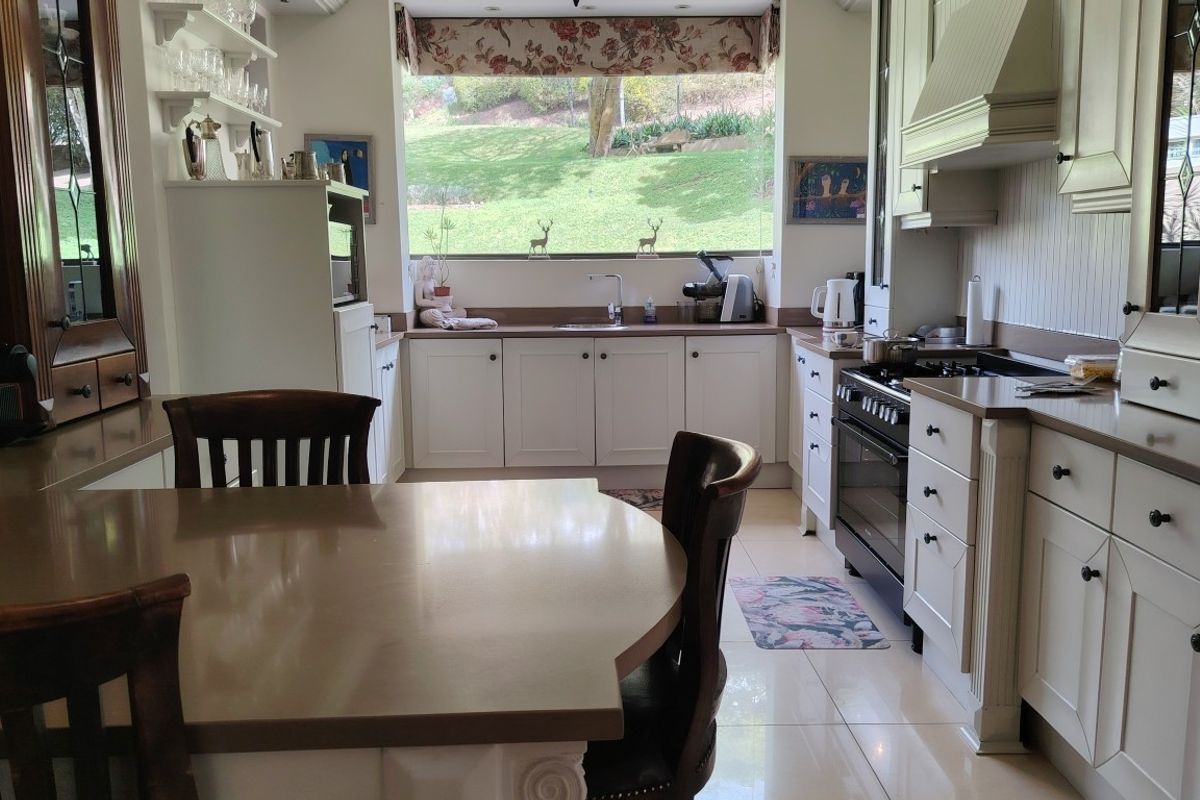 A well-maintained kitchen featuring classic white cabinetry, stone countertops, a gas range, and a large window overlooking the garden.