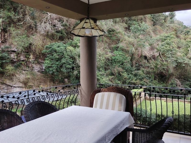 A covered patio featuring a wrought iron balustrade and recessed lighting, offering a scenic view of the surrounding natural landscape and greenery.