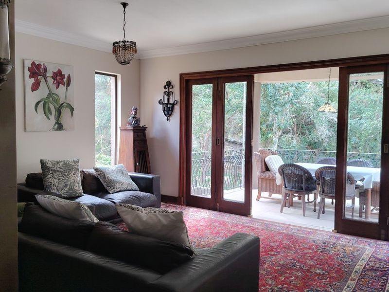 Spacious living room featuring timber-framed sliding doors that open onto a covered patio, providing seamless indoor-outdoor flow and views of the surrounding greenery.
