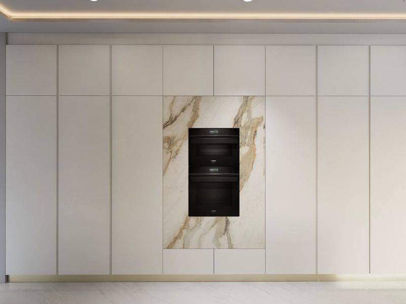 Modern kitchen wall featuring floor-to-ceiling cabinetry, integrated double ovens, and a striking marble feature panel with recessed ceiling lighting.