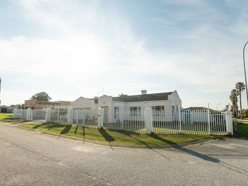 A street-facing view of a single-story residential property featuring a white facade, tiled roof, and secure perimeter fencing with electric wire.