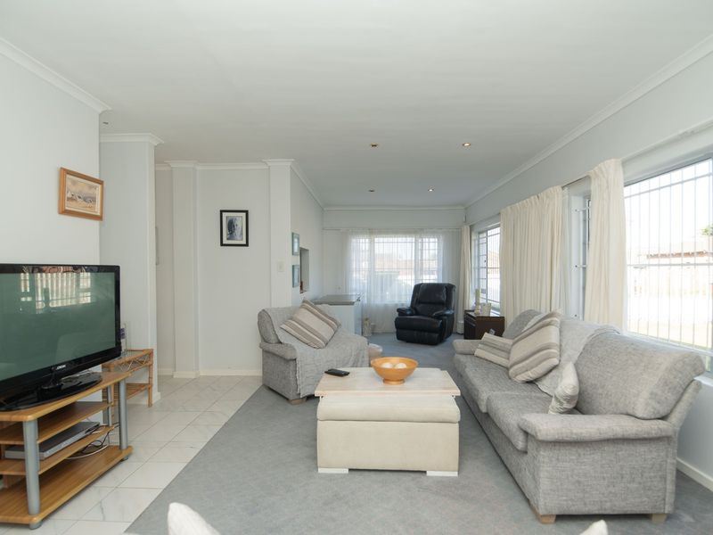 A spacious living room featuring tiled flooring, recessed downlighting, and large windows fitted with security bars, offering a bright and functional living space.