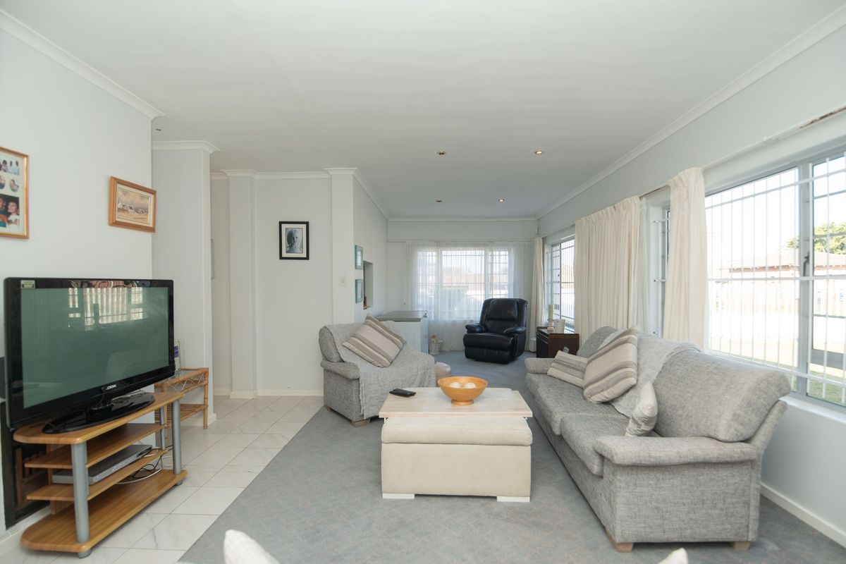 A spacious living room featuring tiled flooring, recessed downlighting, and large windows fitted with security bars, offering a bright and functional living space.