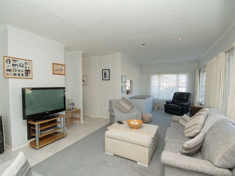 A spacious living room featuring a mix of tiled and carpeted flooring, recessed downlighting, and large windows with security bars.