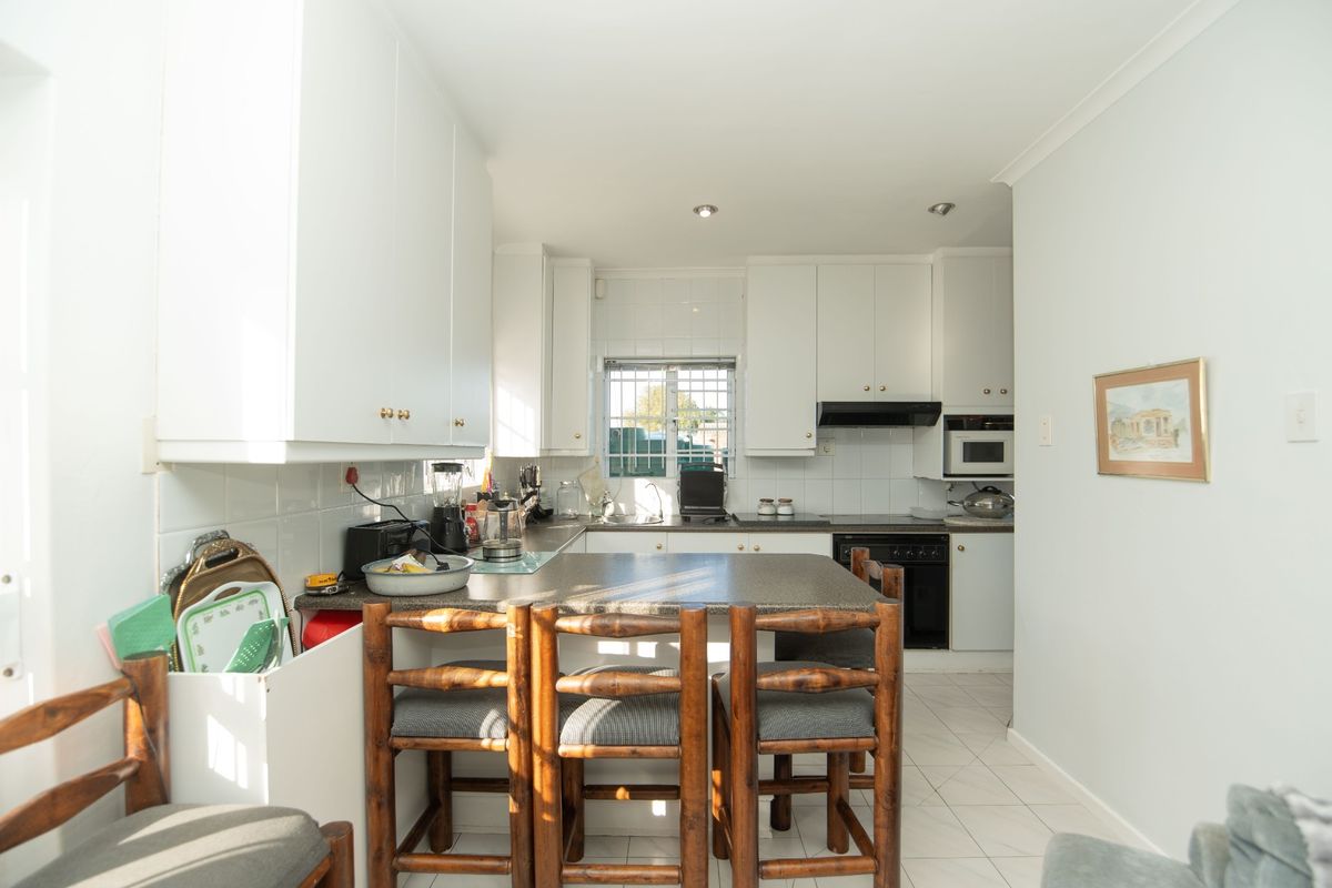 A functional kitchen featuring white cabinetry, tiled backsplash, built-in oven, extractor fan, and a breakfast bar area with tiled flooring.