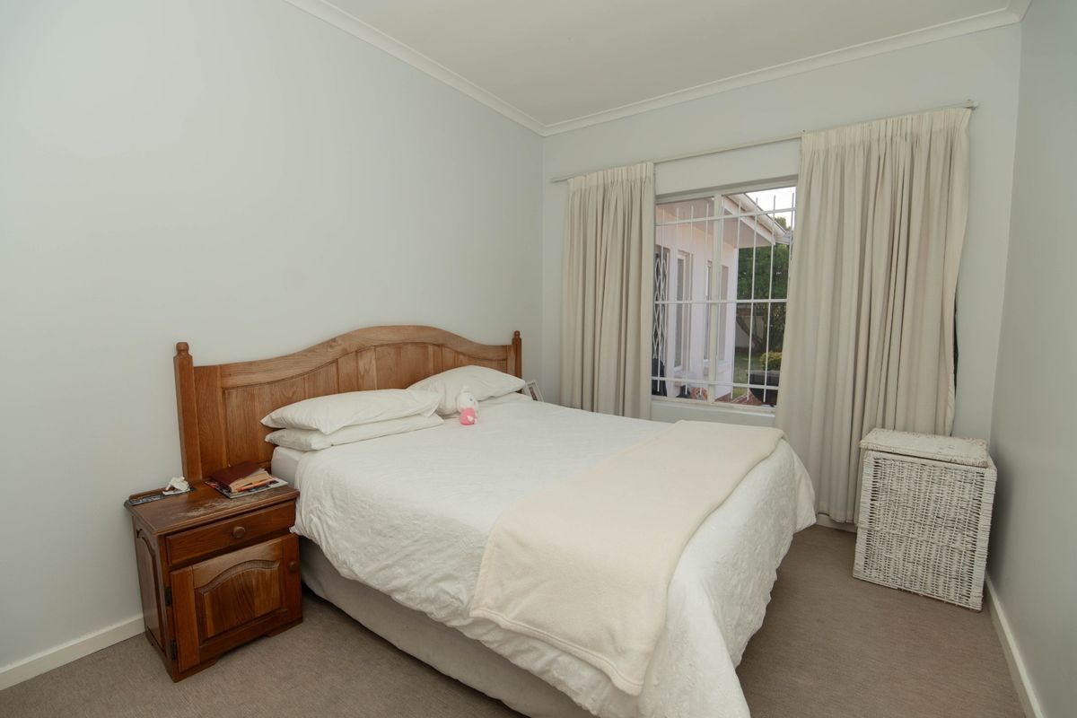 A well-lit bedroom featuring neutral carpet flooring and a window fitted with security bars, offering a functional and comfortable living space.