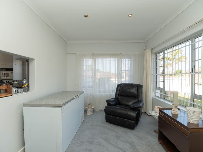 A living area featuring carpeted flooring, recessed downlights, and a convenient serving hatch connecting to the kitchen, with security bars installed on the windows.