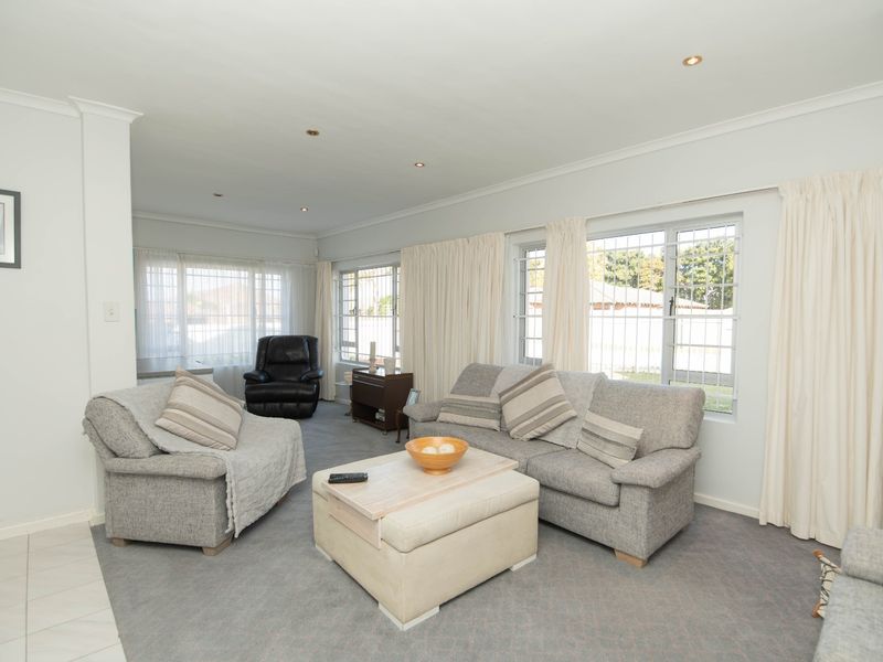 A bright and spacious living room featuring neutral wall tones, recessed downlighting, and large windows fitted with security bars.