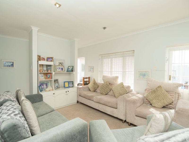 A comfortable living room featuring built-in cabinetry, neutral carpeting, and natural light through a window and glass-paneled door with security gate.