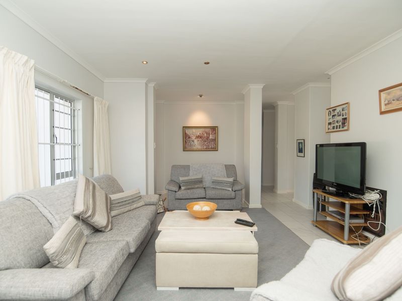 A well-lit living room featuring neutral walls, tiled flooring, and recessed downlighting, providing a comfortable and functional space for relaxation.