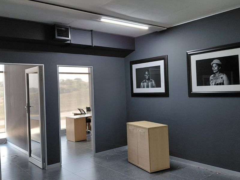 A modern office space featuring dark grey walls, tiled flooring, and glass panel doors leading to an adjacent workspace.