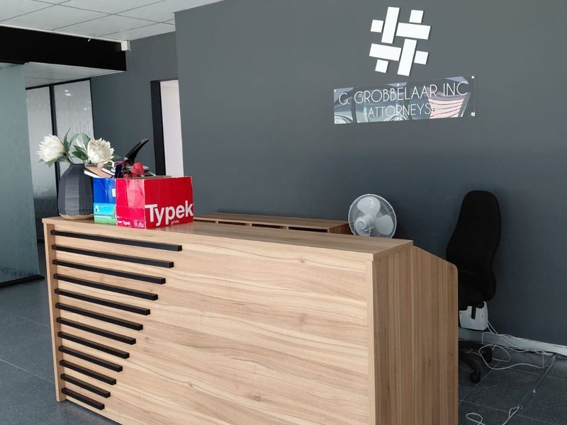 Professional office reception area featuring a modern wood-finish reception desk, dark grey accent wall, and tiled flooring.