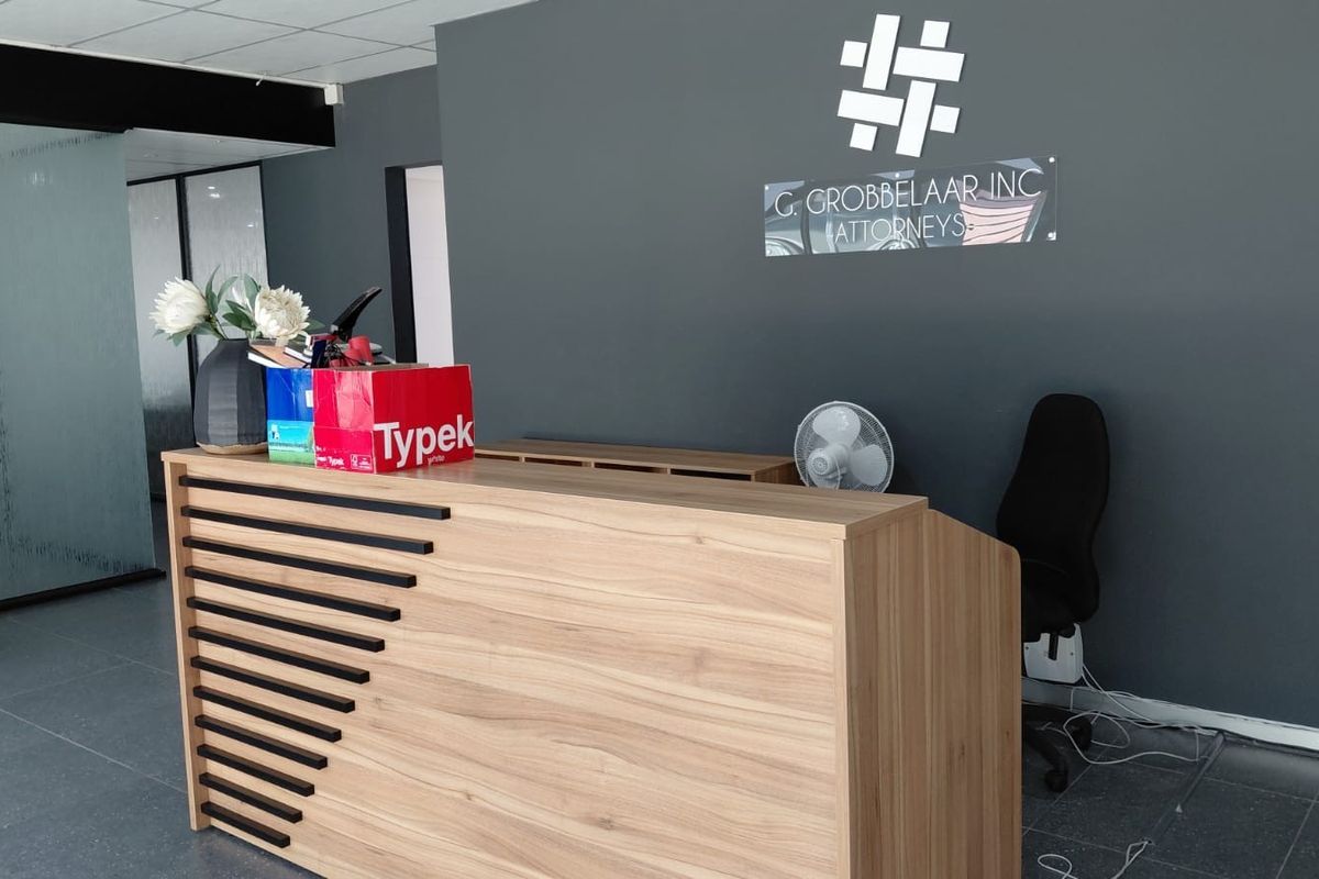 Professional office reception area featuring a modern wood-finish reception desk, dark grey accent wall, and tiled flooring.