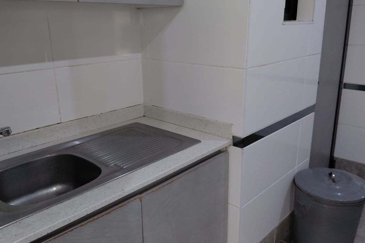 A compact kitchenette area featuring a stainless steel sink, stone countertop, and tiled wall finishes, showing signs of wear on the cabinetry.
