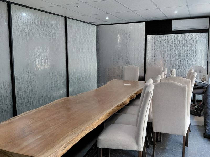 A modern office meeting room featuring frosted glass partitions, a suspended ceiling with recessed lighting, and a split-system air conditioning unit.