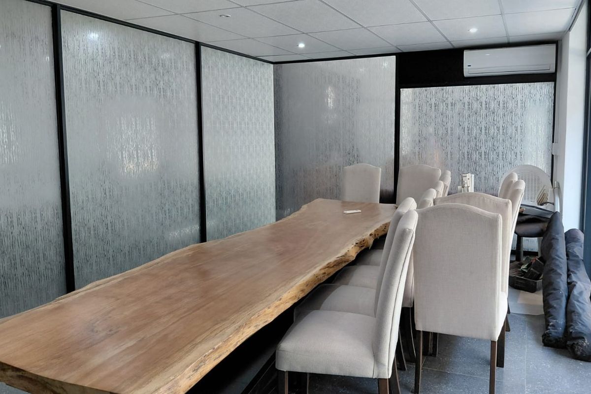 A modern office meeting room featuring frosted glass partitions, a suspended ceiling with recessed lighting, and a split-system air conditioning unit.