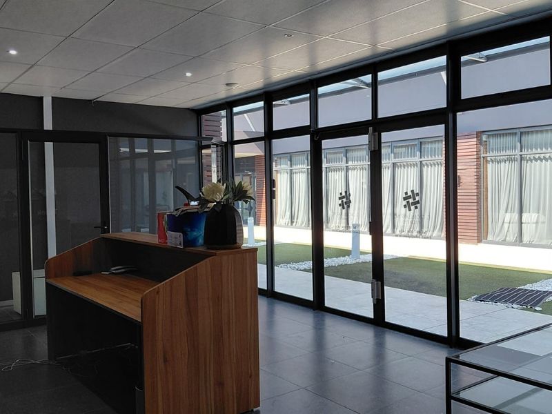 Modern office reception area featuring floor-to-ceiling glass walls, tiled flooring, and a built-in reception desk with views of an outdoor courtyard.