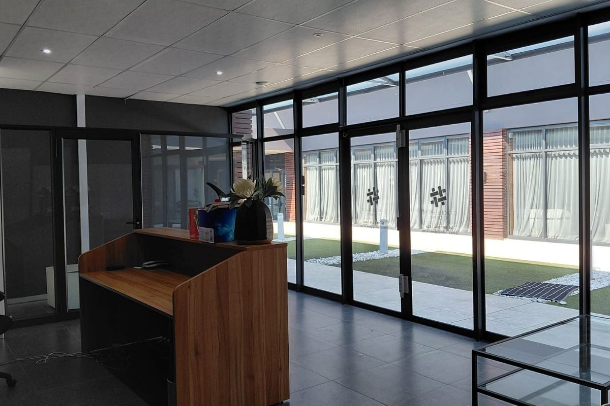 Modern office reception area featuring floor-to-ceiling glass walls, tiled flooring, and a built-in reception desk with views of an outdoor courtyard.