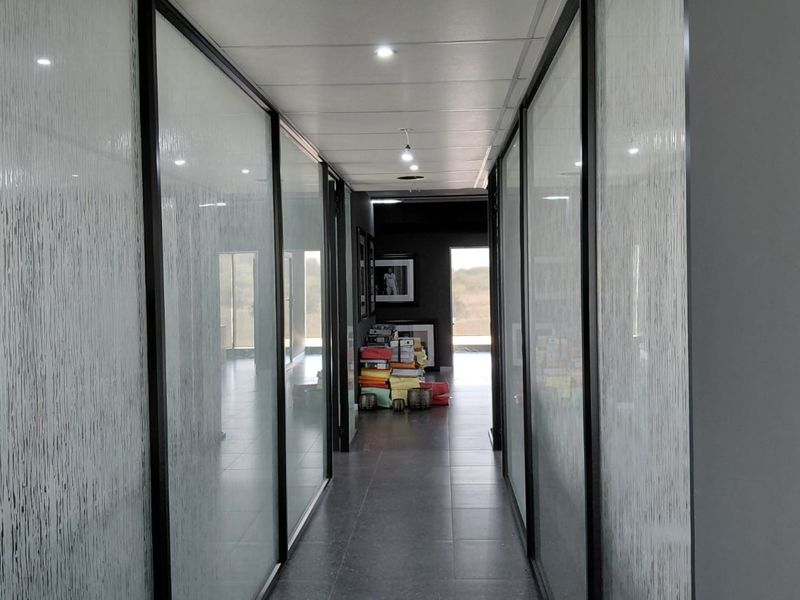 A modern office hallway featuring glass partition walls, tiled flooring, and recessed ceiling lighting, creating a professional and bright workspace environment.