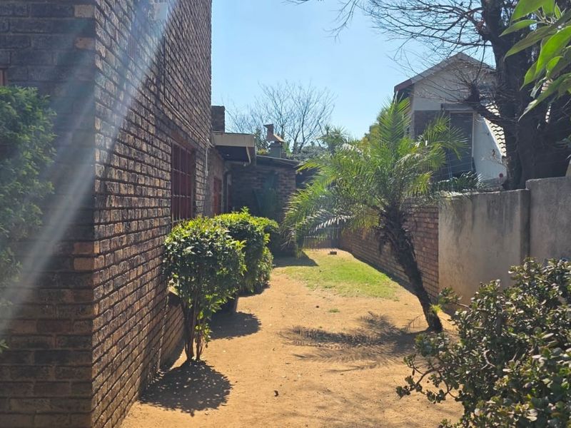 A side view of the property featuring a face brick exterior wall, a narrow garden path, and a boundary wall.