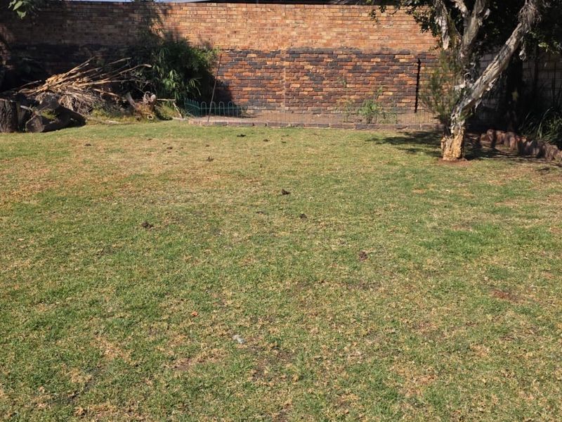 A spacious backyard featuring a large lawn area enclosed by a brick boundary wall, offering potential for landscaping and outdoor improvement.