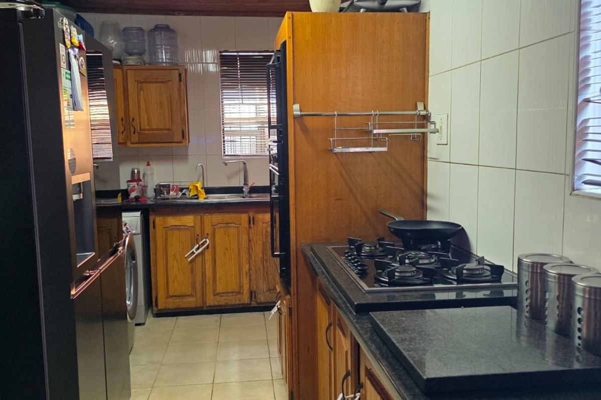 A functional kitchen featuring wooden cabinetry, granite countertops, a gas hob, and a built-in oven with tiled splashbacks.