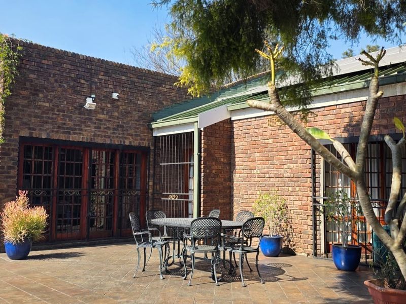 A spacious outdoor patio area featuring face brick walls, tiled flooring, and secure timber-framed access doors, overlooking a pool area.