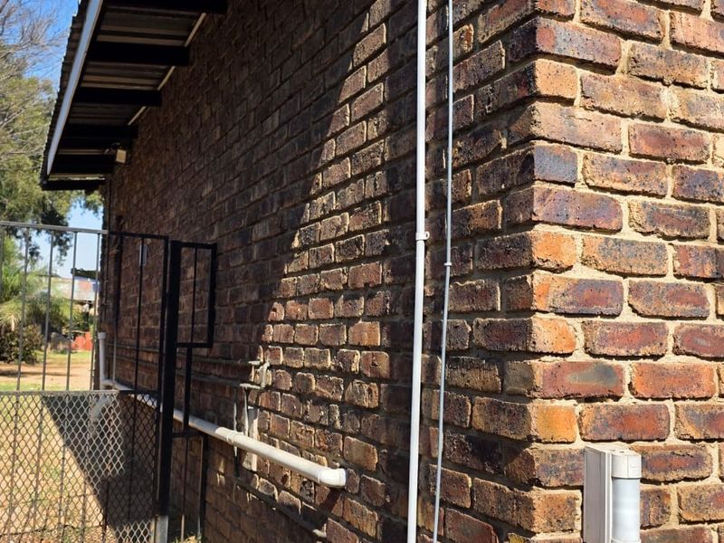 A side view of the property featuring face brick exterior walls, metal window frames with security bars, and external utility fixtures.