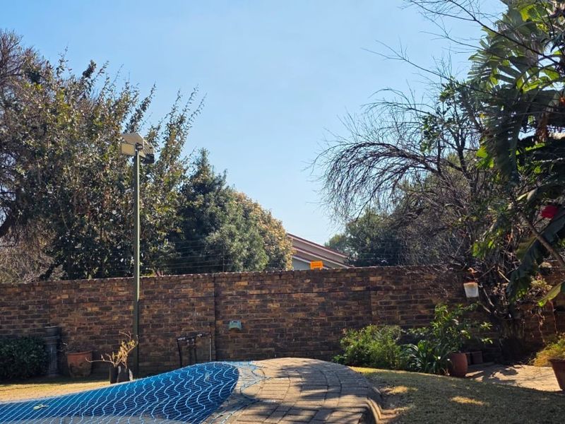 Outdoor pool area featuring a paved surround, brick boundary wall with electric fencing, and established garden landscaping.