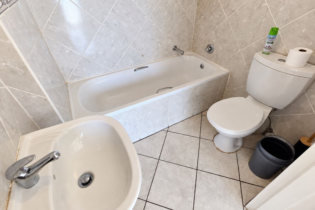 A functional bathroom featuring a bathtub, pedestal basin, and toilet with neutral ceramic wall and floor tiling.