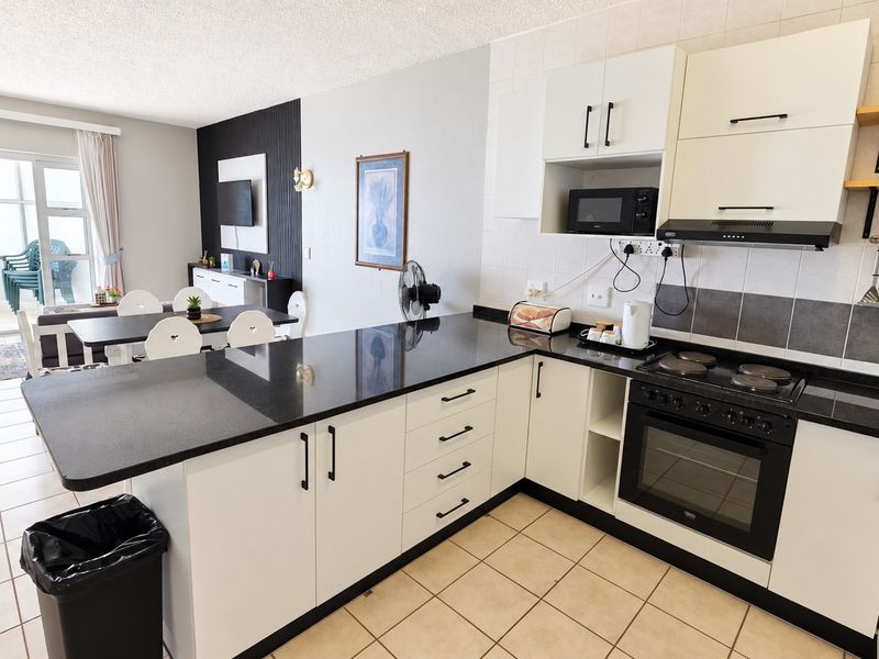 Open-plan kitchen and living area featuring modern white cabinetry, black granite countertops, built-in appliances, and direct access to a balcony through sliding doors.
