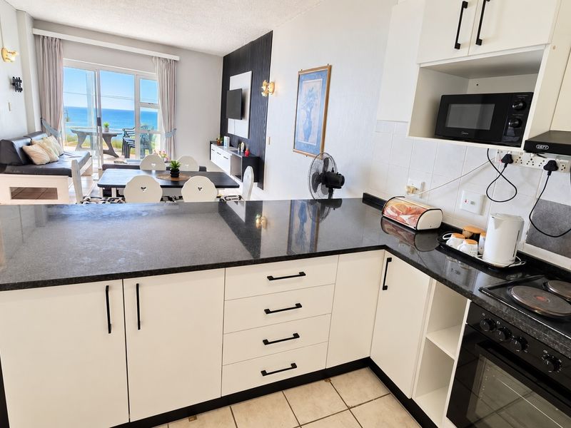 Open-plan kitchen and living area featuring modern white cabinetry, granite countertops, and direct access to a balcony with ocean views.