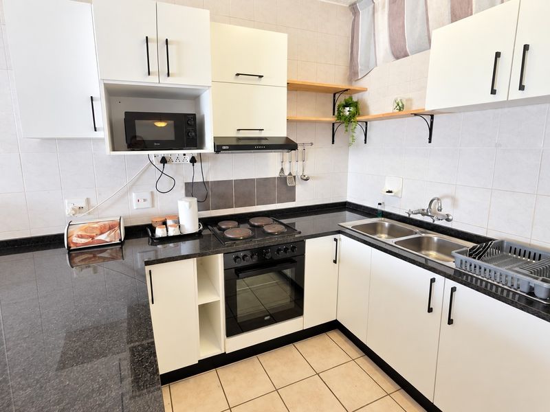 A functional kitchen featuring white cabinetry, dark granite countertops, a double basin sink, and integrated electric cooking appliances with a tiled backsplash.