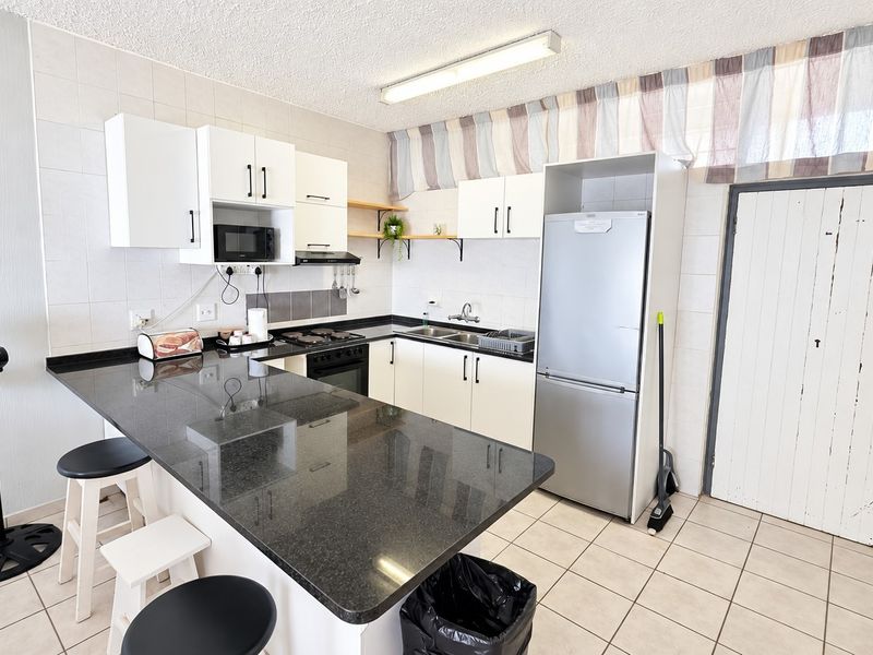 Functional kitchen featuring granite countertops, built-in cabinetry, a hob, oven, and tiled flooring, offering a practical layout for daily meal preparation.