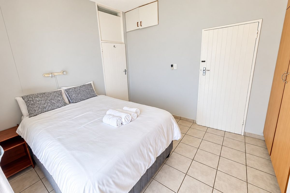 A functional bedroom featuring tiled flooring, built-in storage cupboards, and overhead cabinetry, providing a clean and practical living space.