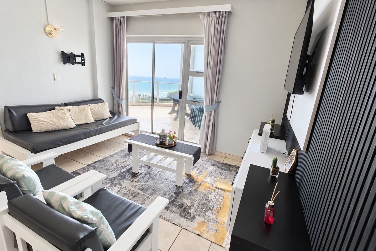 Bright living room featuring tiled floors, modern slatted wall detailing, and direct access to a balcony with ocean views.