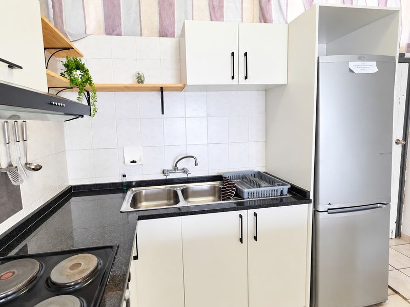 Compact kitchen featuring white cabinetry, granite countertops, a double sink, and a built-in electric hob with an extractor fan.