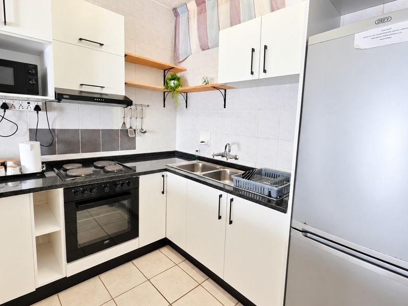 A functional kitchen featuring white cabinetry, granite countertops, a double basin sink, and integrated appliances including an electric hob and oven.