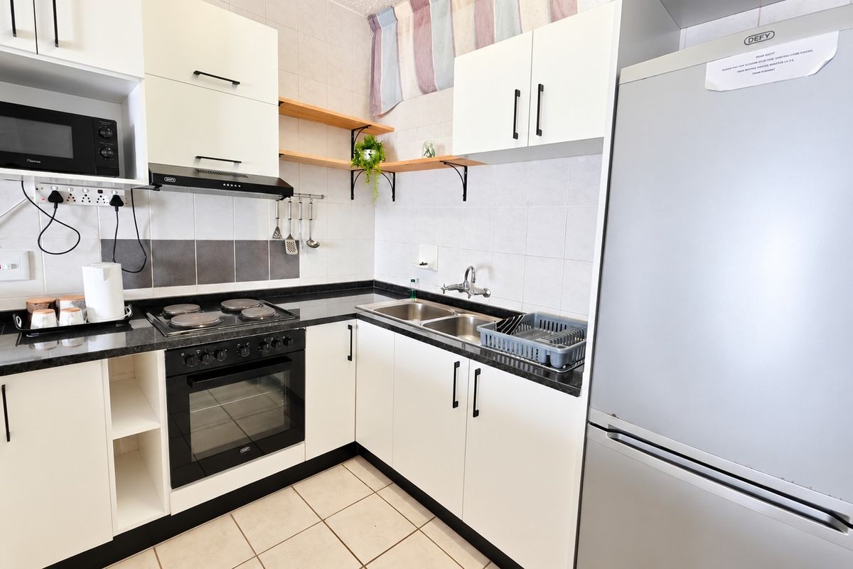 A functional kitchen featuring white cabinetry, granite countertops, a double basin sink, and integrated appliances including an electric hob and oven.
