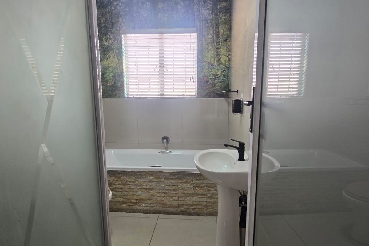 A functional bathroom featuring a pedestal basin, a built-in bathtub with stone-cladding detail, and tiled flooring, viewed through a frosted glass door.