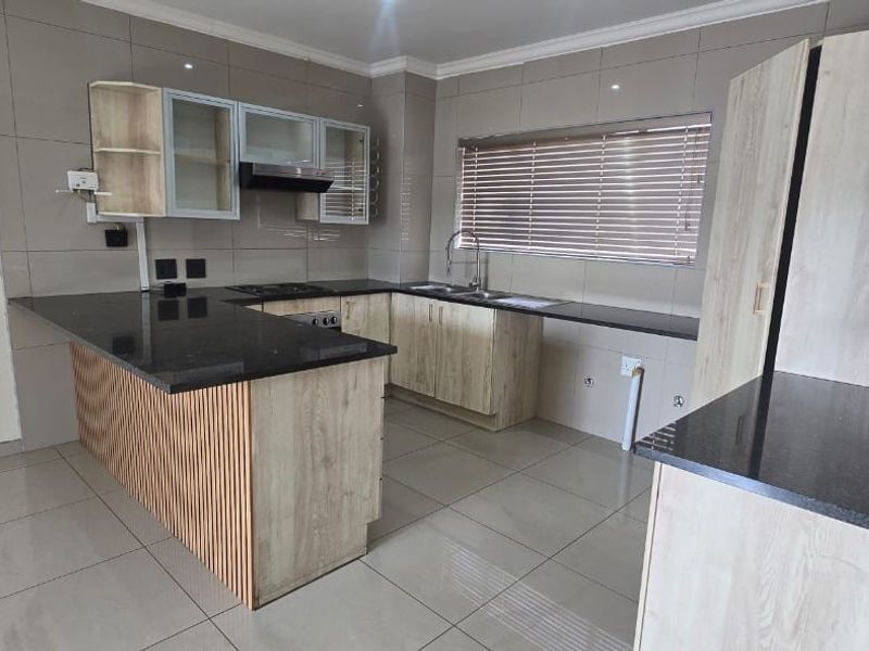 Modern kitchen featuring light wood-finish cabinetry, dark granite countertops, integrated appliances, and tiled flooring in a clean, open-plan layout.