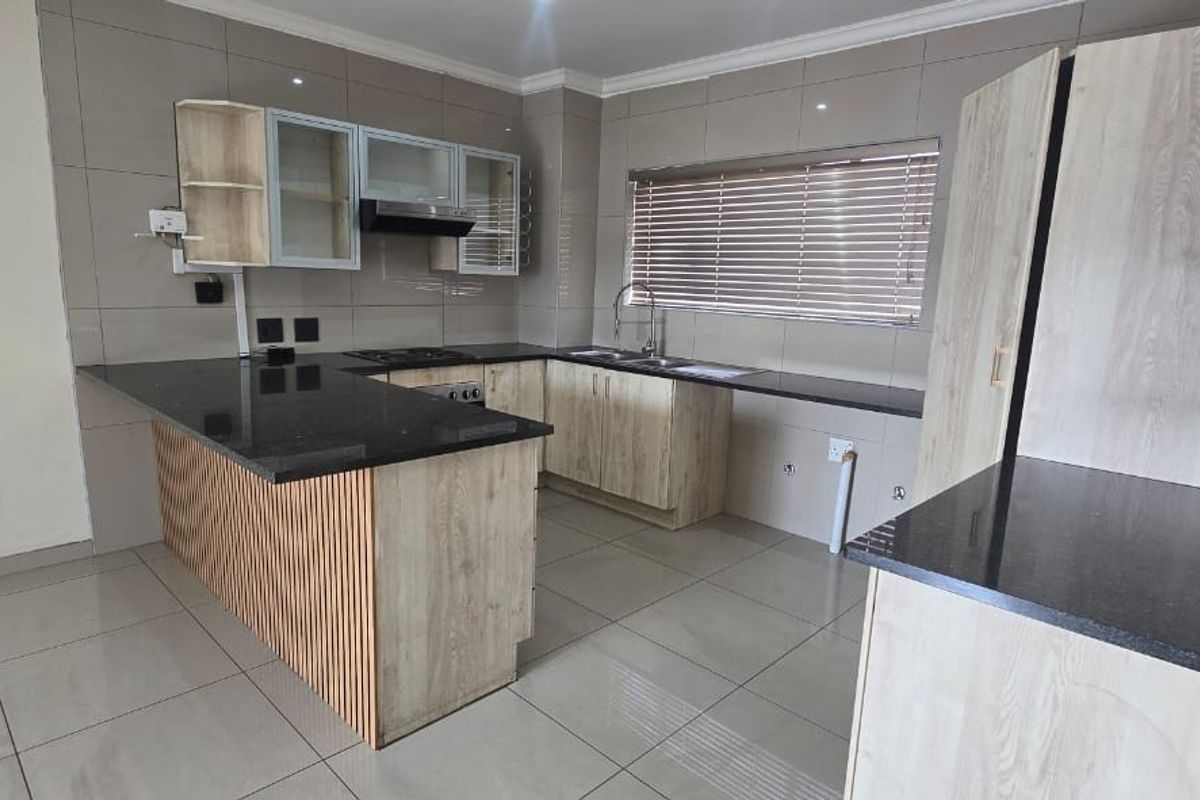 Modern kitchen featuring light wood-finish cabinetry, dark granite countertops, integrated appliances, and tiled flooring in a clean, open-plan layout.
