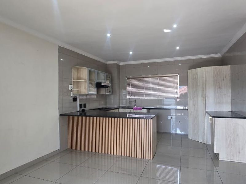 Modern kitchen featuring granite countertops, ample built-in cabinetry, a central island, and tiled finishes throughout, offering a clean and functional culinary space.
