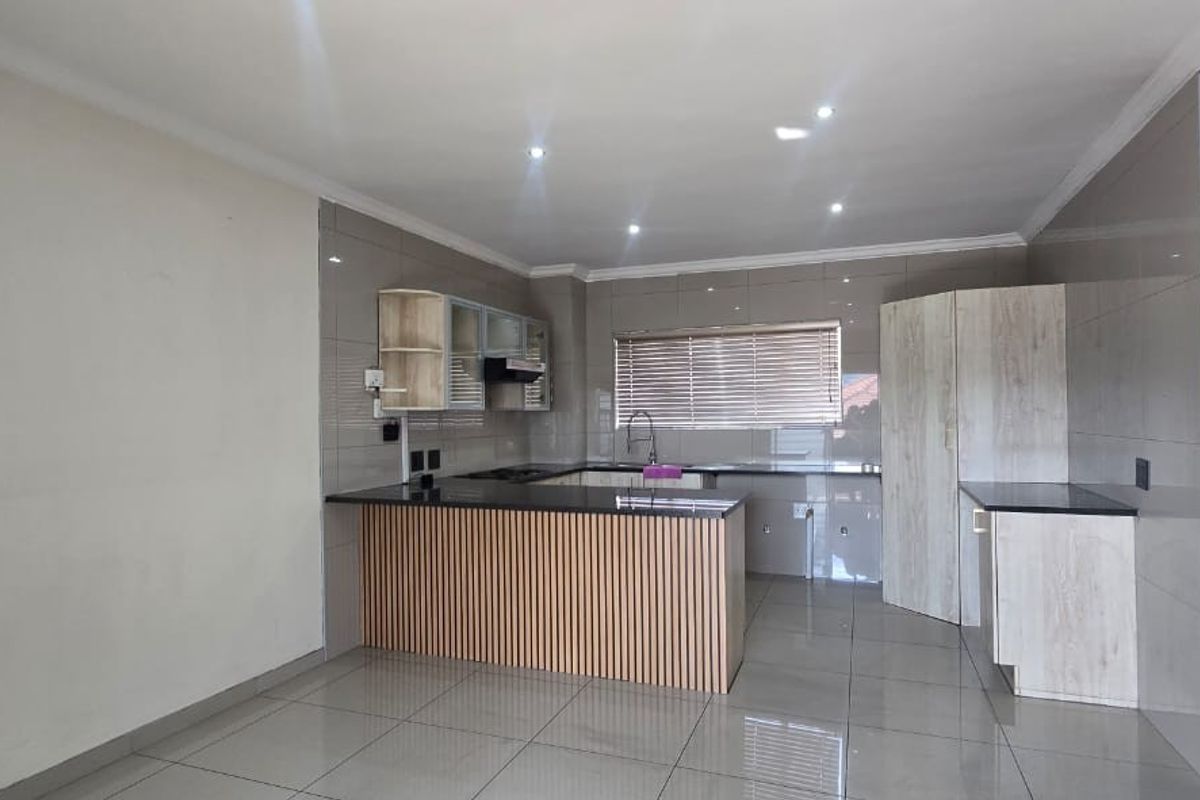 Modern kitchen featuring granite countertops, ample built-in cabinetry, a central island, and tiled finishes throughout, offering a clean and functional culinary space.