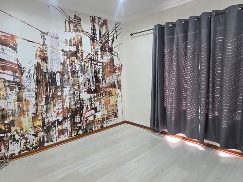 An empty bedroom featuring light-toned laminate flooring and a decorative city-themed feature wall, providing a neutral base for personalization.