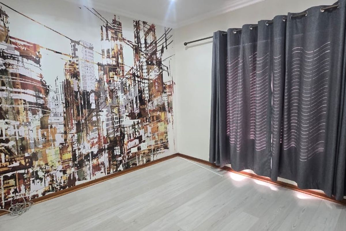 An empty bedroom featuring light-toned laminate flooring and a decorative city-themed feature wall, providing a neutral base for personalization.